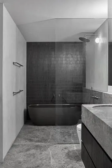 Dark bathroom renovation with a black freestanding bath, charcoal wall tiles, stone floor and walk in shower