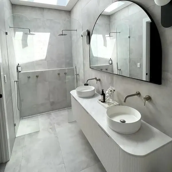 Bathroom with a fluted double vanity, vessel basins, black arched mirror and walk in shower