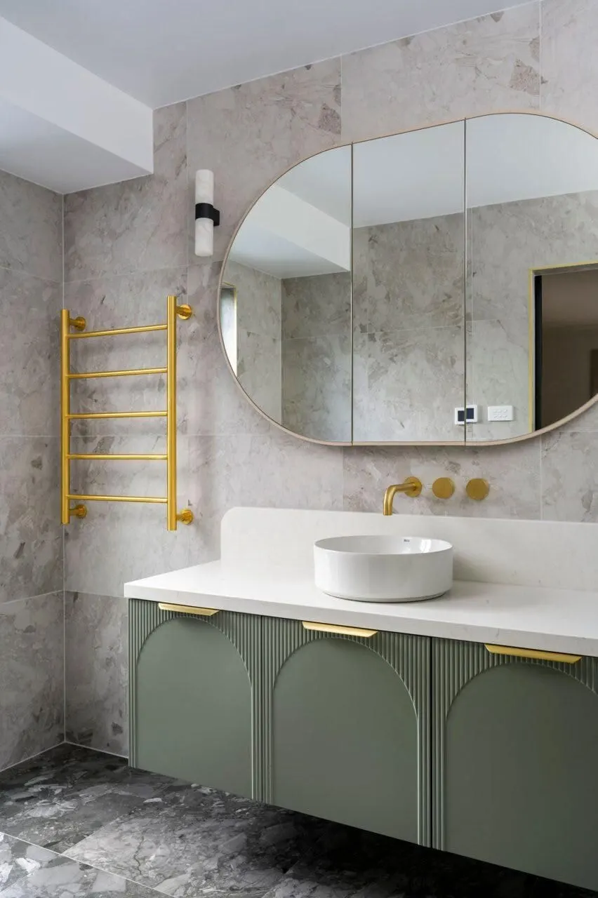Bathroom with a sage green arched vanity, brushed brass tapware, heated towel rail and terrazzo floor