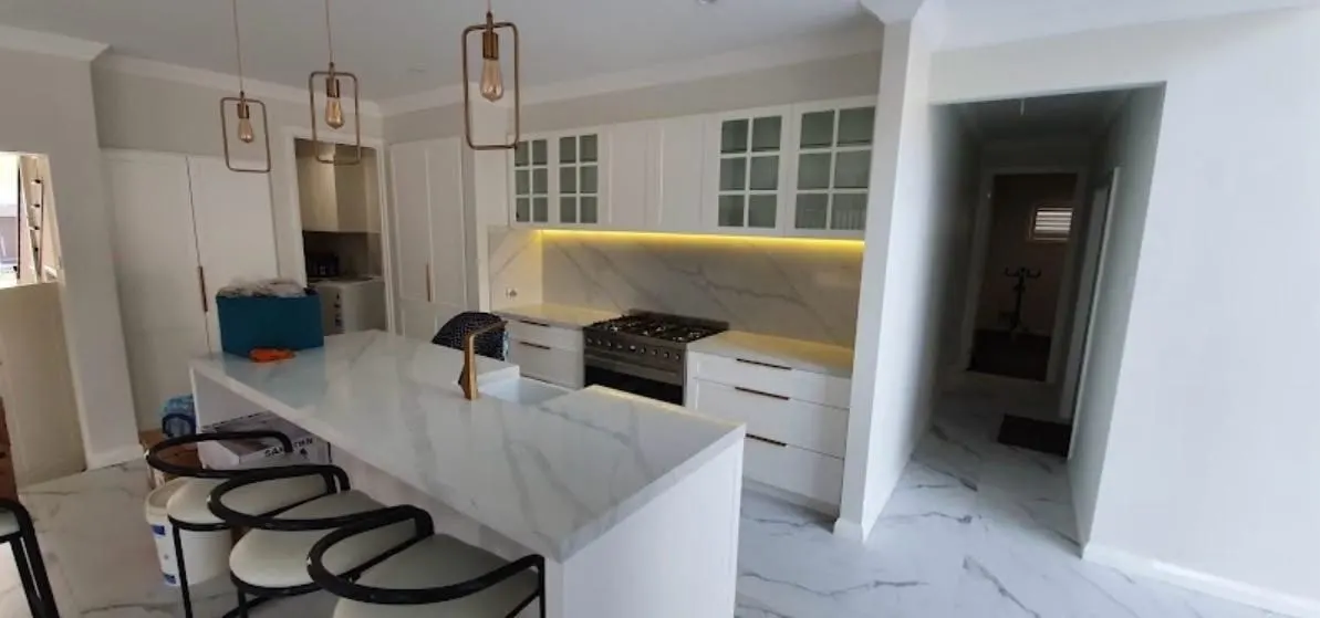 Kitchen renovation with a marble look island bench, copper pendant lights, glass display cabinets and LED strip lighting