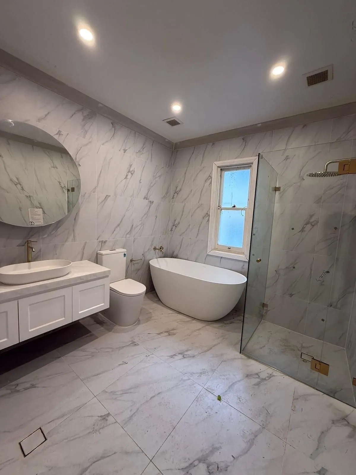 Marble look bathroom with a freestanding bath, shaker vanity, round mirror and frameless shower screen