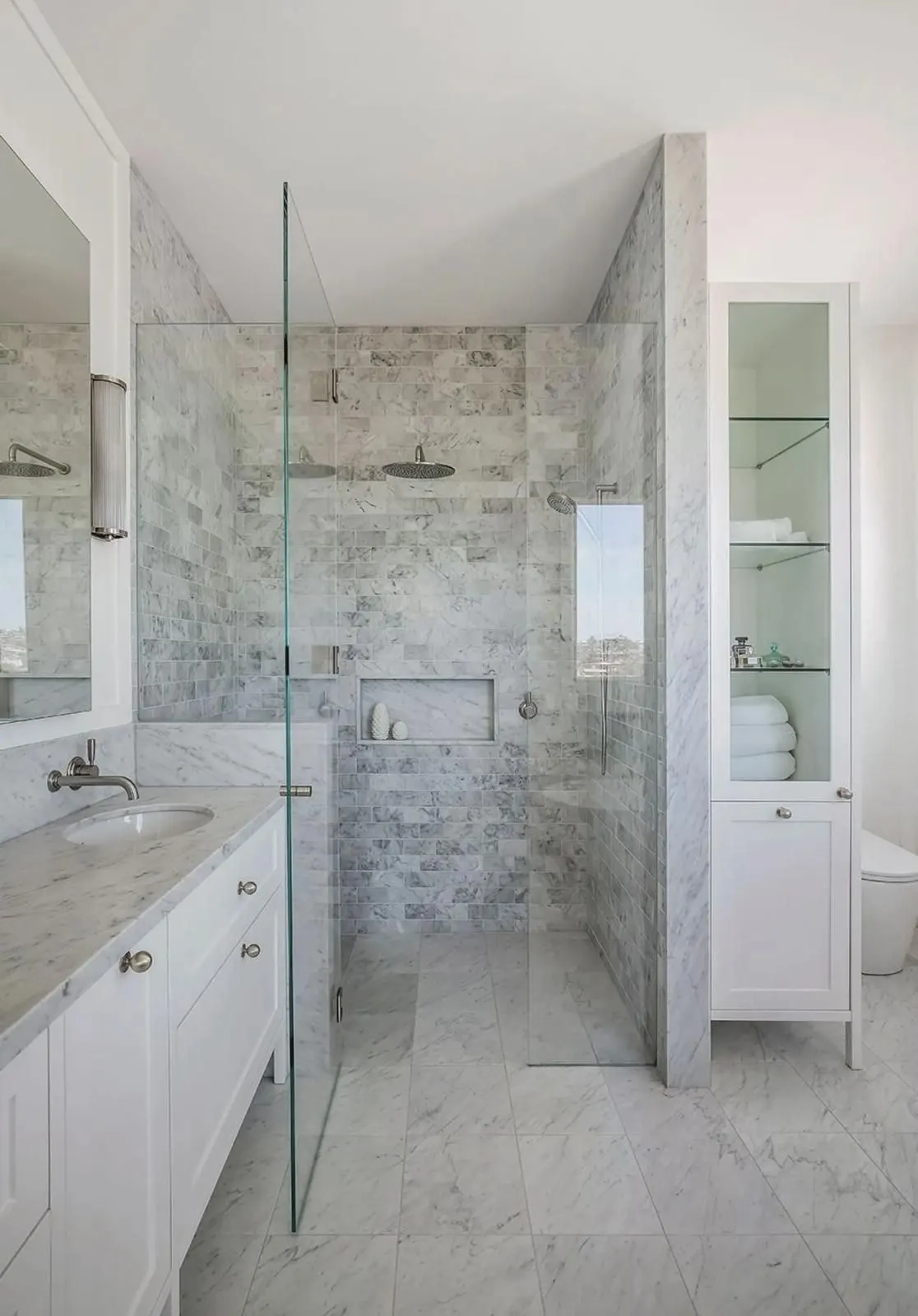 Bright bathroom renovation with a marble look walk in shower, frameless glass panel, recessed niche and white shaker vanity