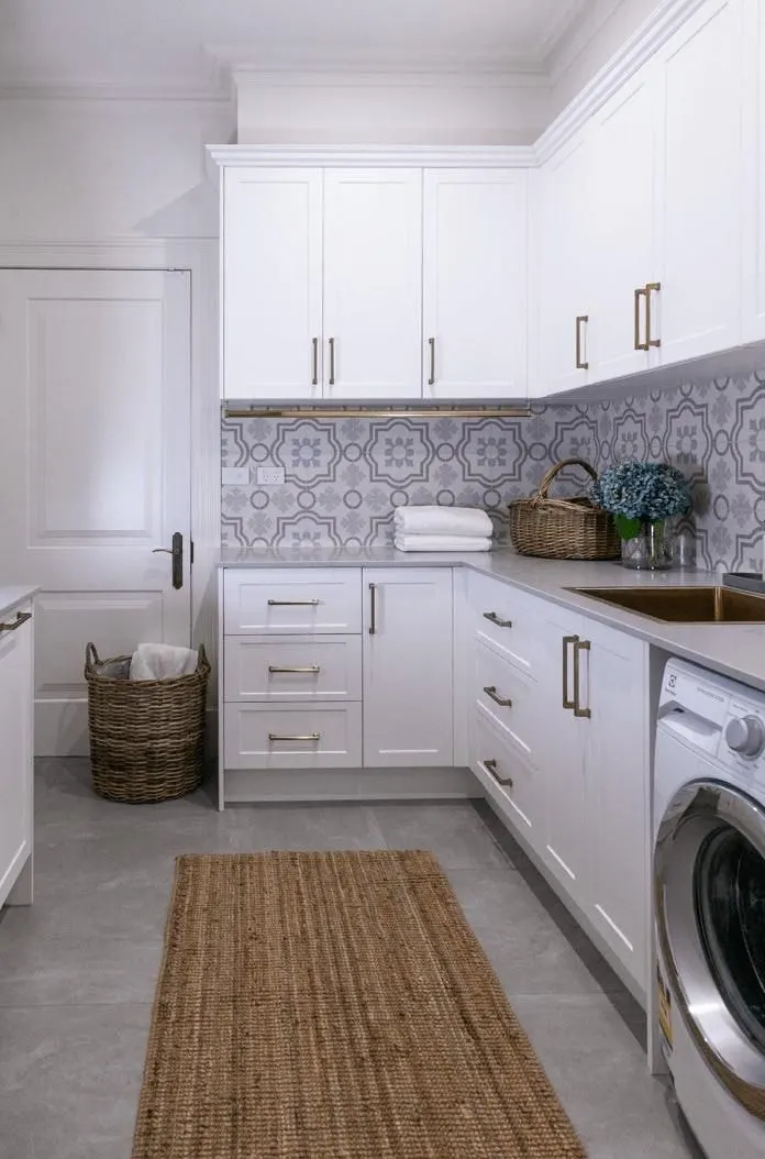 White shaker laundry with patterned splashback tiles, brass handles, front loading washer and plenty of storage