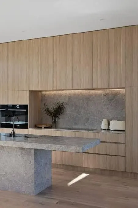 Floor to ceiling timber veneer kitchen joinery with integrated ovens and a natural stone island