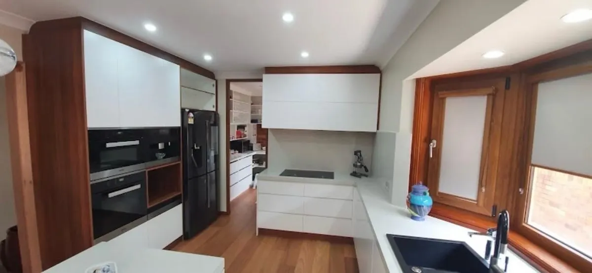 Timber and white custom cabinetry with integrated ovens, tall storage and a long stone benchtop