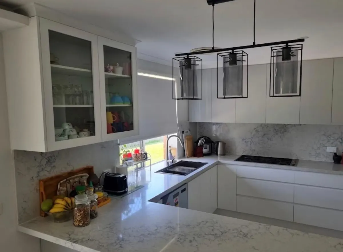 U shaped kitchen with stone benchtops, glass display cabinets, black pendant lights and a window splashback
