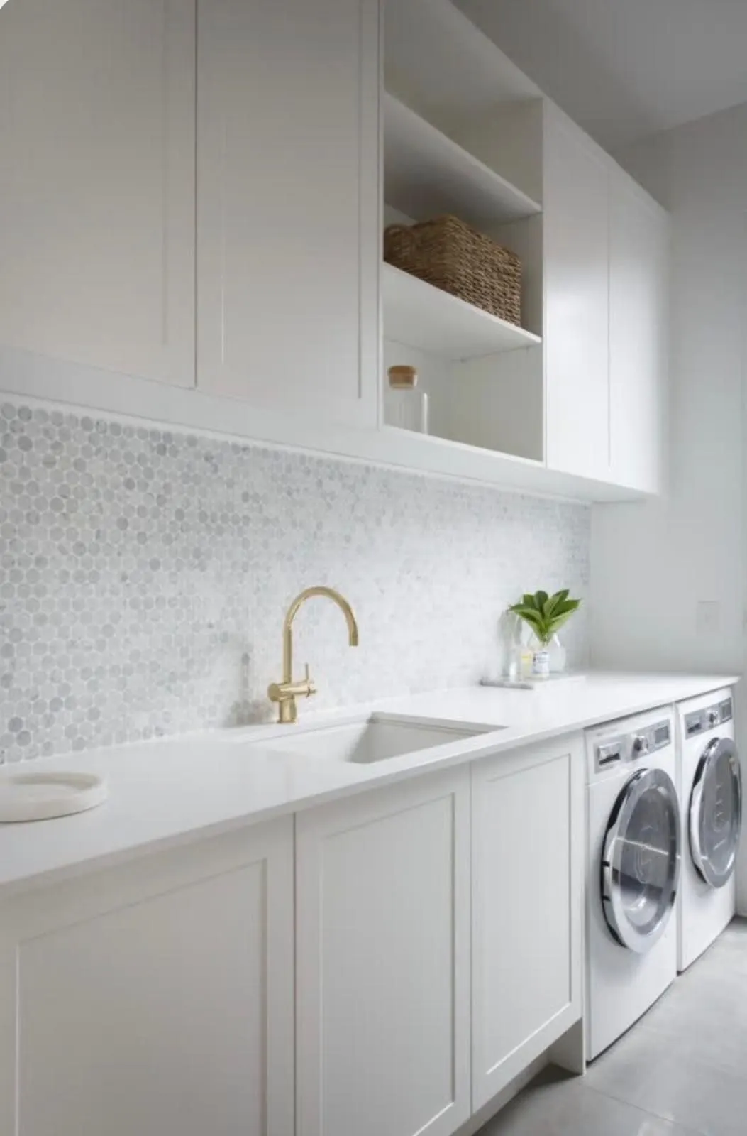 White laundry with a marble hexagon splashback, brass tap, open shelving and front loading machines